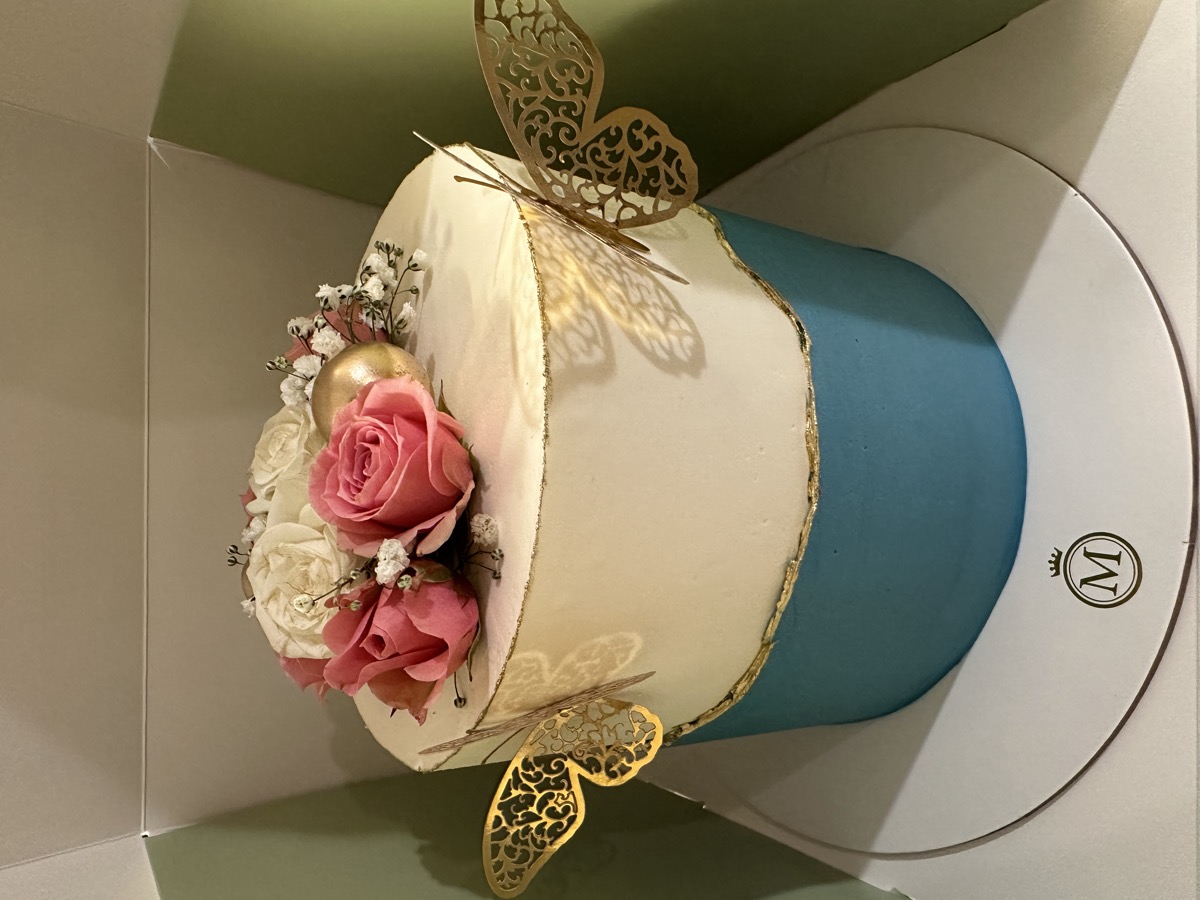 Elegant white and blue cake topped with roses and gold butterfly decorations