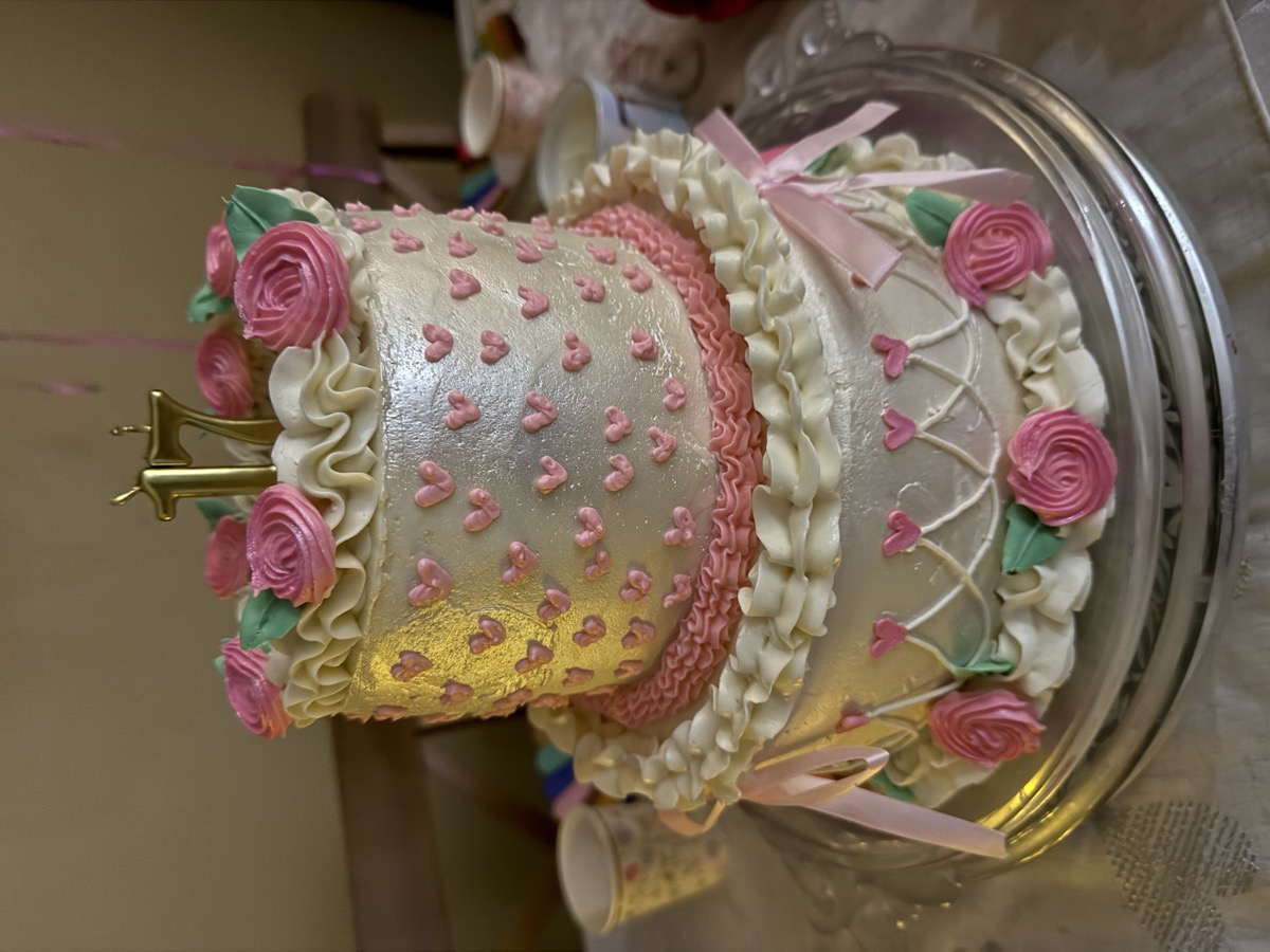 Two-tier pink and white cake with hearts, roses, and ribbon details