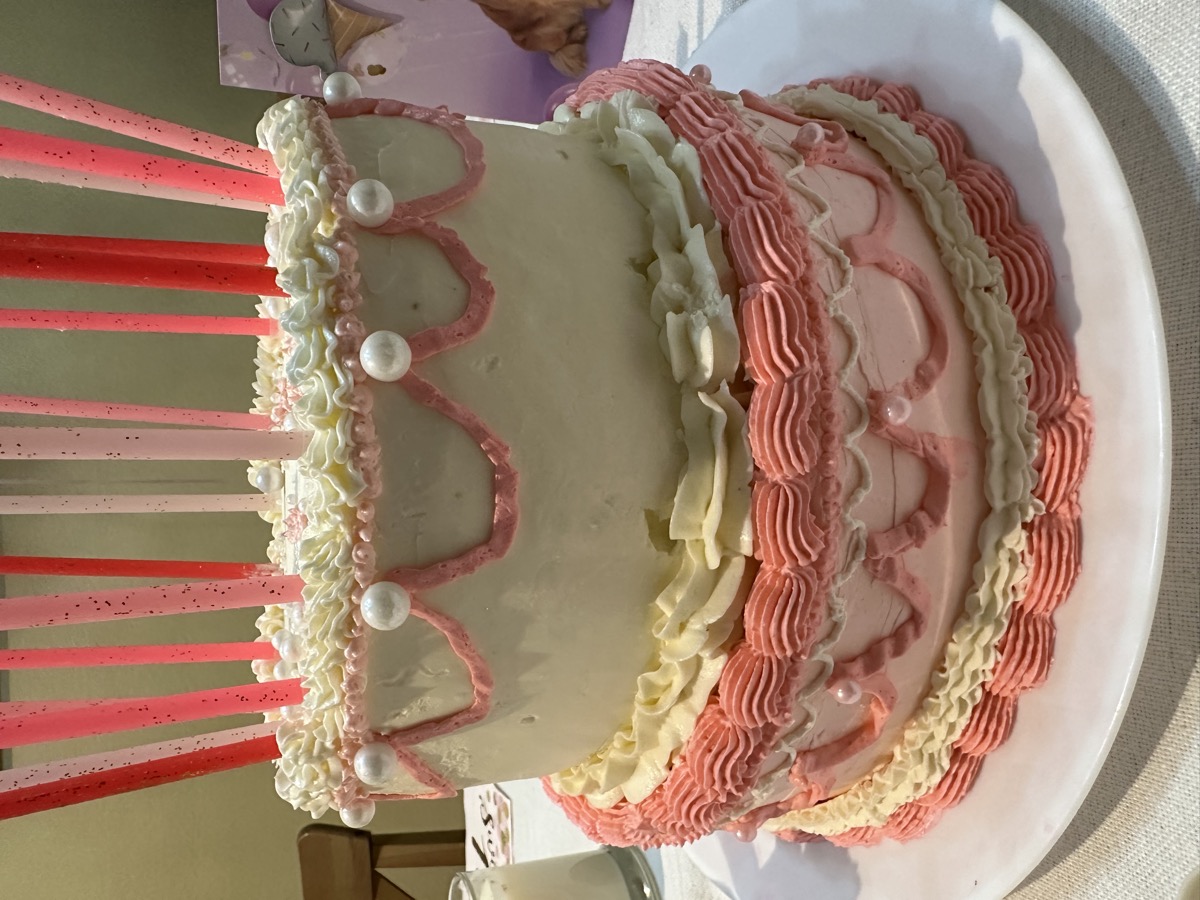 Two-tier vintage pink and white cake with pearl details and candles