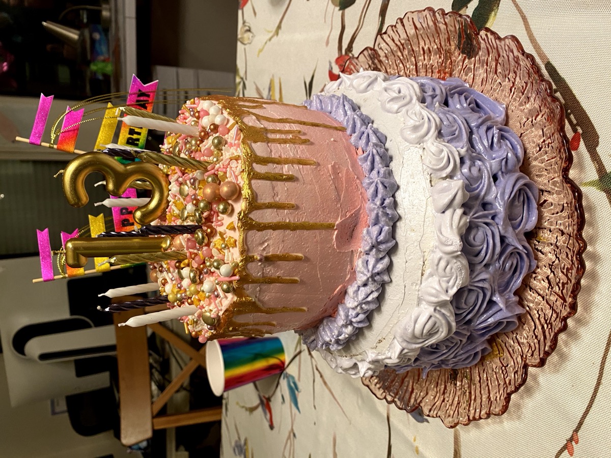 Colorful pink and purple tiered drip cake with gold accents and rosettes